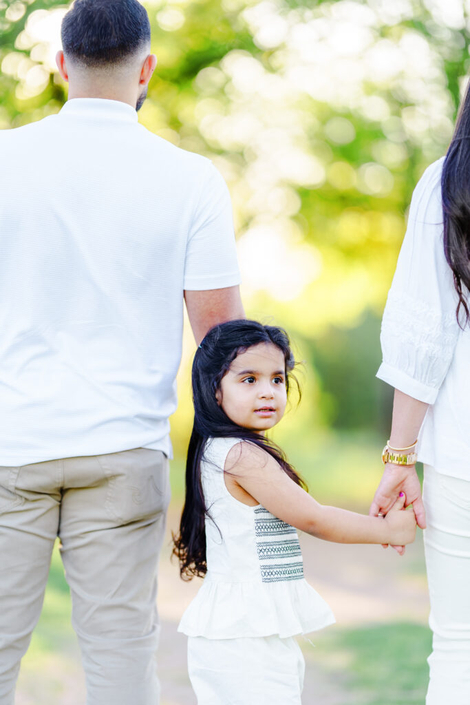 Young girl holding her mother’s hand, gazing softly at the camera capturing stillness and quiet connection during a family session at Parker Rose Gardens in Dallas.