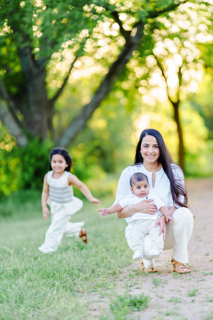 Mother and daughters running barefoot through sunlit grass, capturing movement and joy during a storytelling family photography session at Parker Rose Gardens in Dallas.
