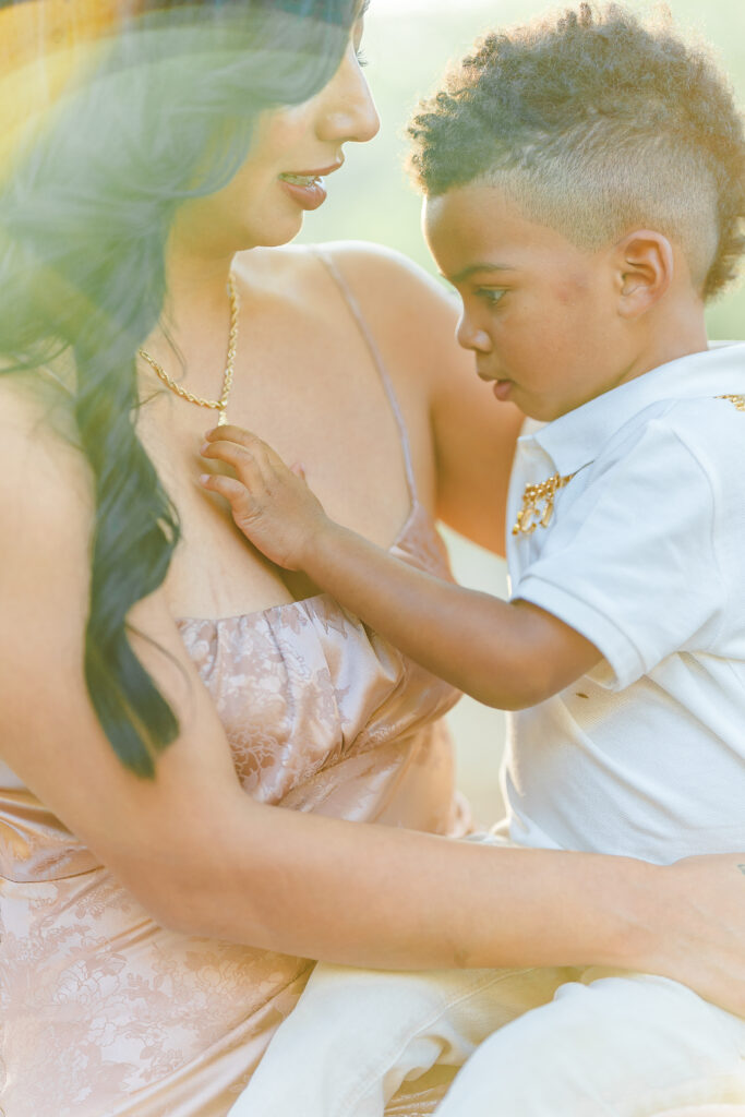 Young child resting with his mother while gently holding her necklace outdoors