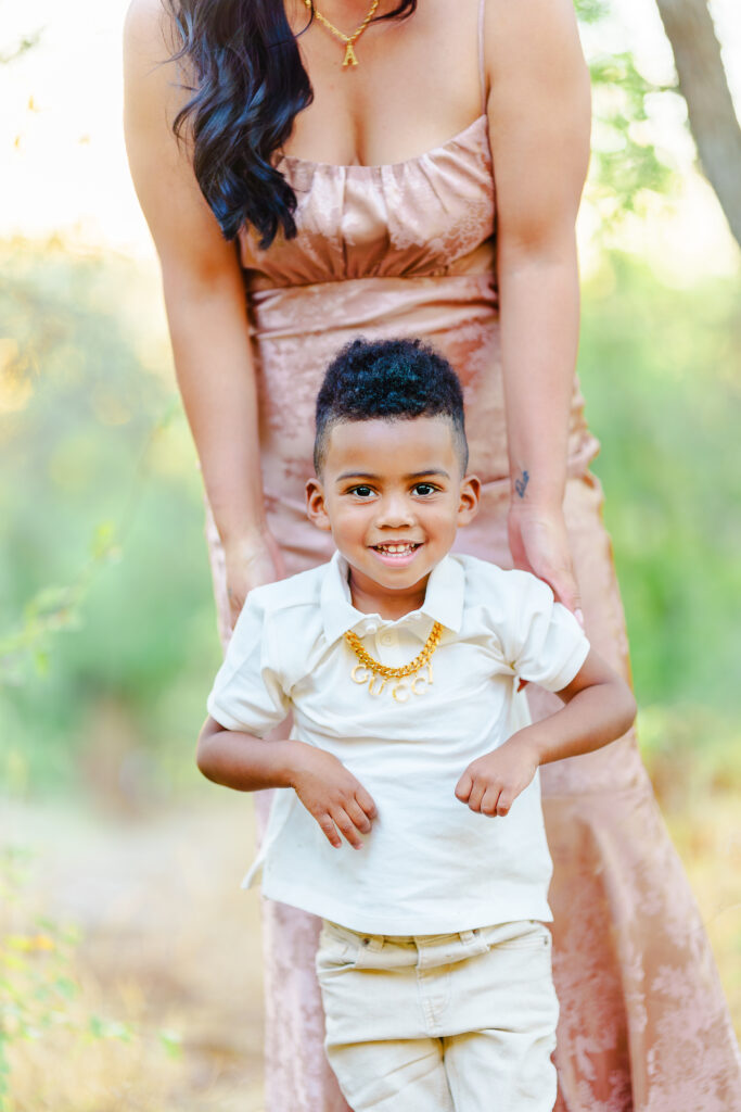 Young boy smiling while standing with his mother outdoors in natural light