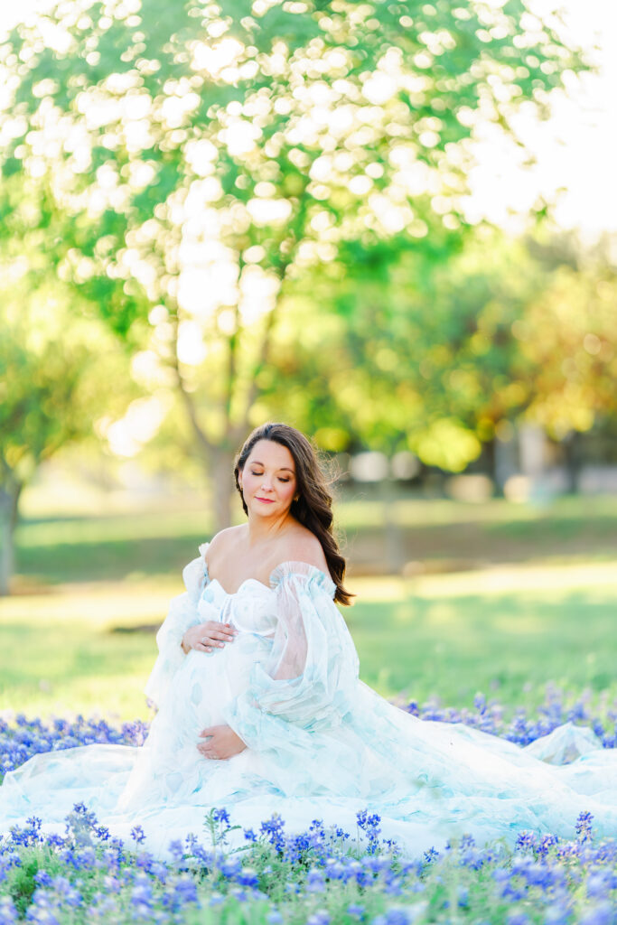 An expecting mother nestled in a field of bluebonnets for her maternity session near Dallas, Texas